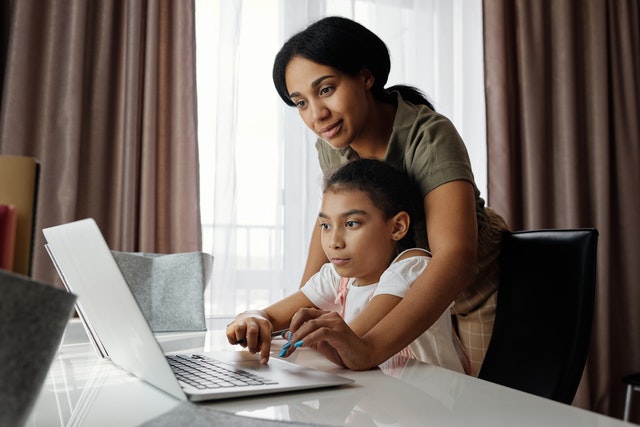 a parent helping girl child with online leaerning on a laptop